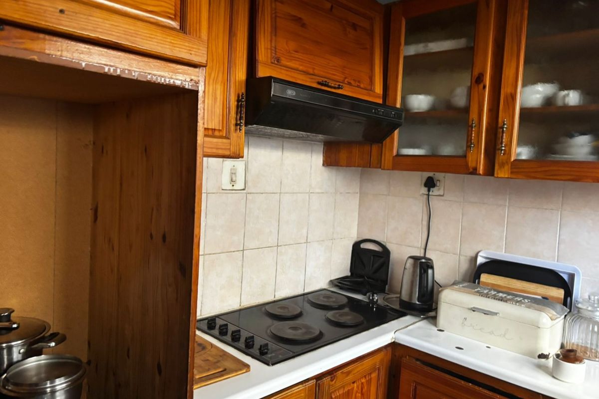 A dated kitchen featuring traditional wooden cabinetry, a tiled backsplash, and a built-in electric hob with an extractor fan.