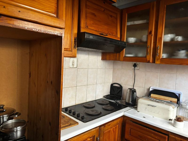 A dated kitchen featuring traditional wooden cabinetry, a tiled backsplash, and a built-in electric hob with an extractor fan.