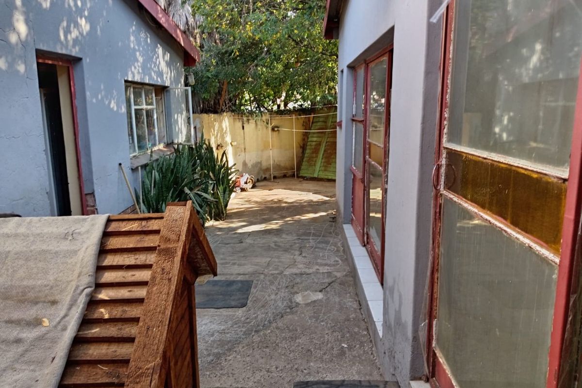 A narrow rear courtyard area featuring concrete paving, boundary walls, and access points to the main dwelling through metal-framed glass doors.