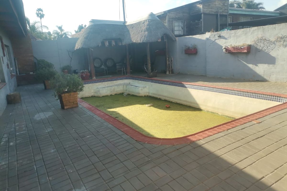 Outdoor pool area featuring a paved patio, a thatched lapa, and a swimming pool requiring maintenance and cleaning.