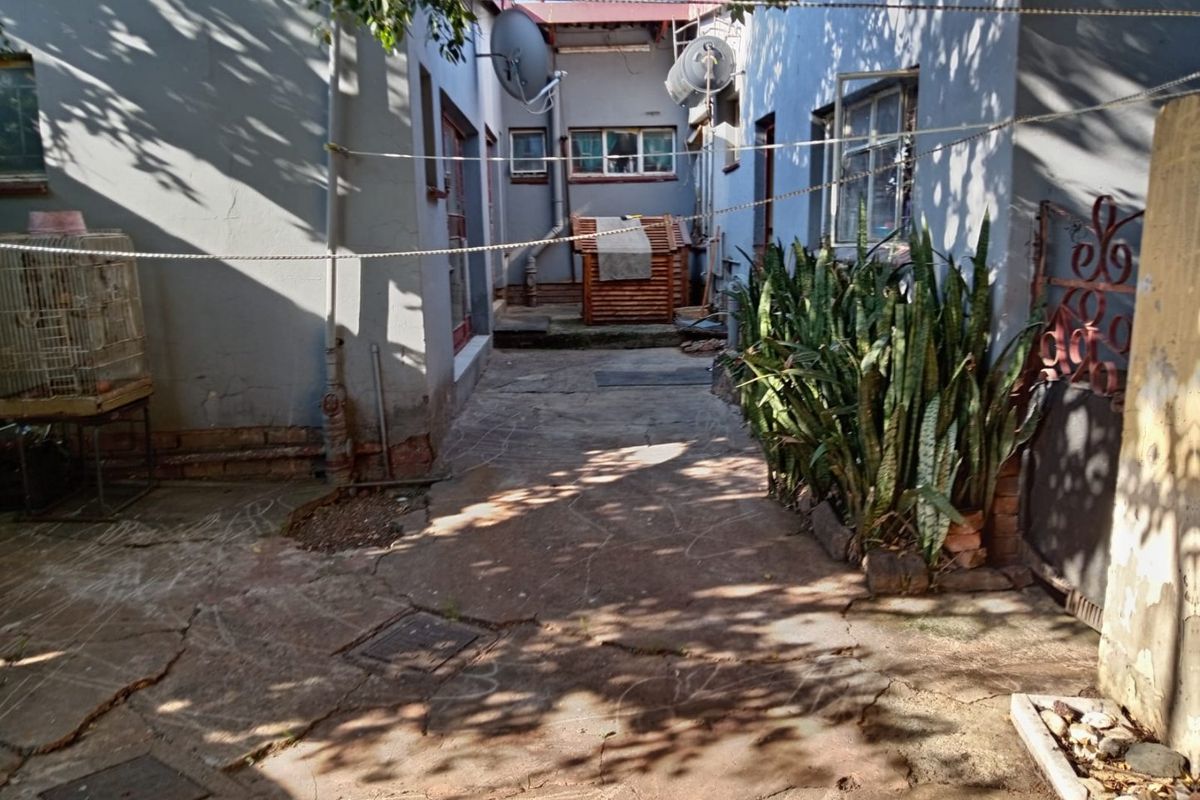 A rear courtyard area featuring paved surfaces, external building access, and established perimeter planting, requiring maintenance and cosmetic updates.