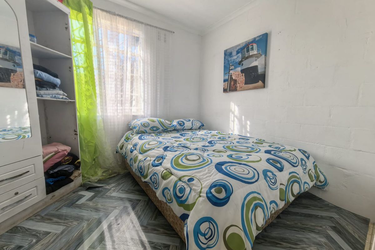 A compact bedroom featuring a built-in wardrobe and tiled flooring, with visible blockwork walls requiring cosmetic attention.