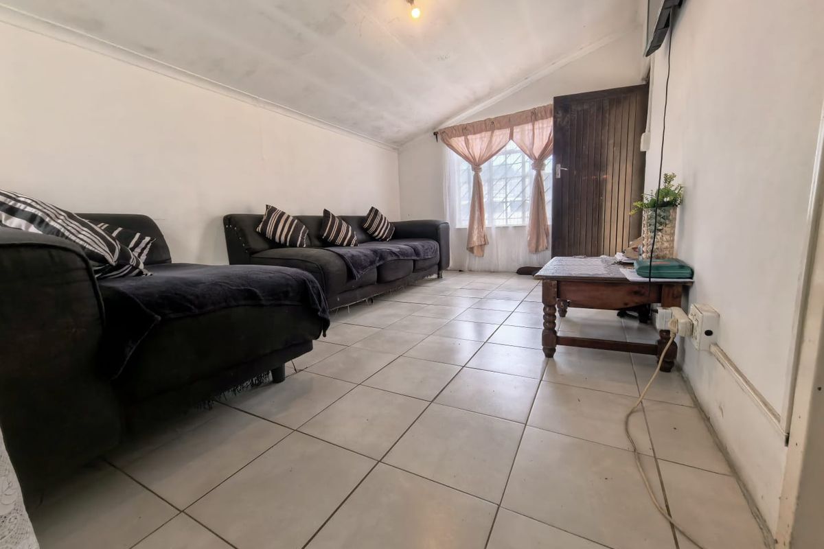 A living room featuring tiled flooring and a sloped ceiling, offering a functional space with potential for cosmetic updates.