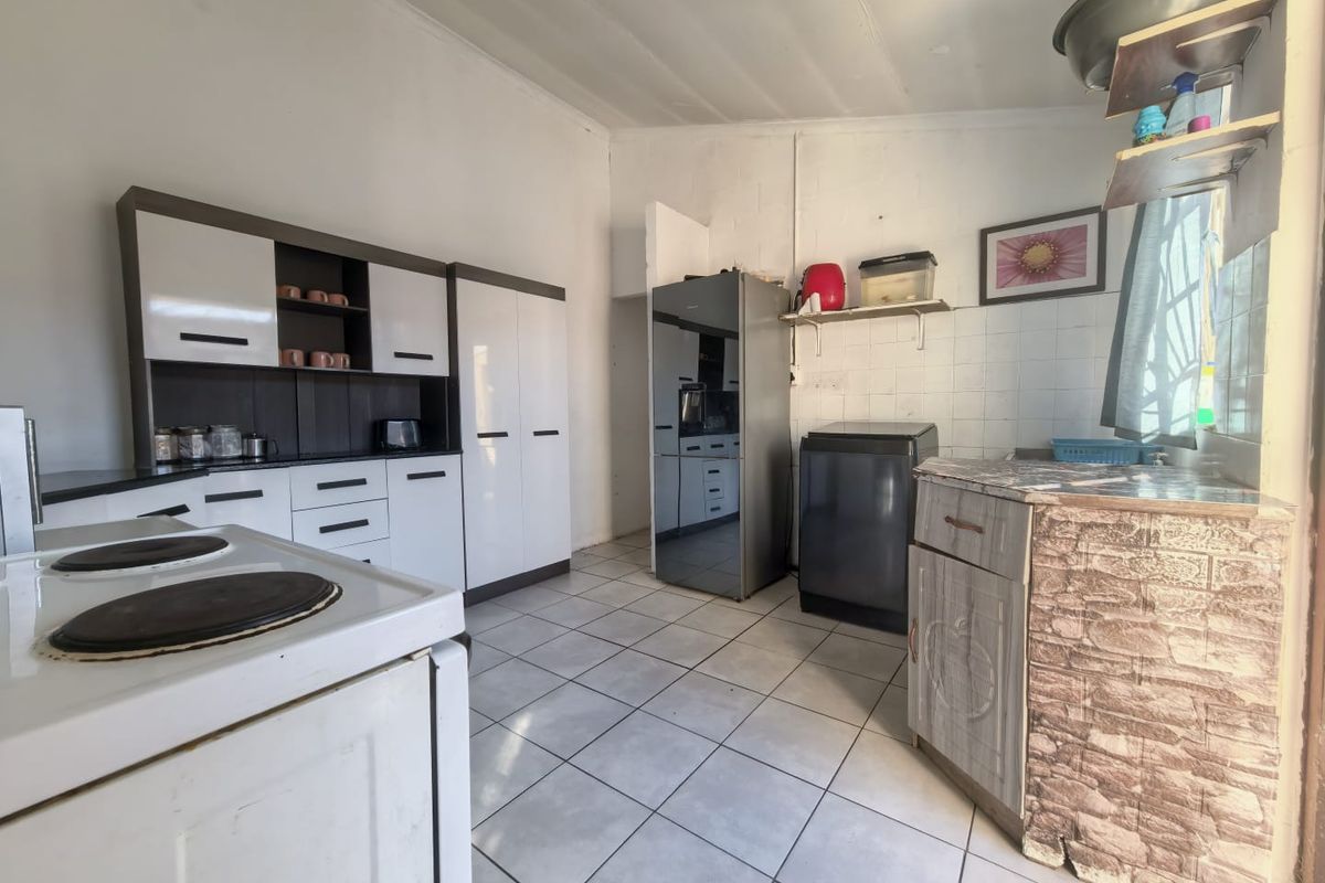 A functional kitchen featuring built-in cabinetry, tiled flooring, and a tiled splashback, offering a practical layout with potential for cosmetic updates.