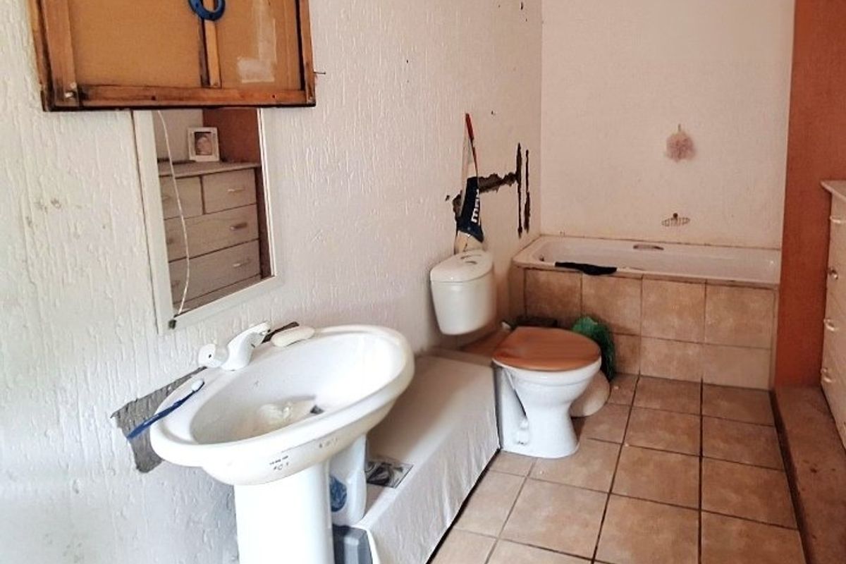 A dated bathroom featuring a pedestal basin, toilet, and built-in bathtub, currently requiring significant renovation and repair to wall finishes.
