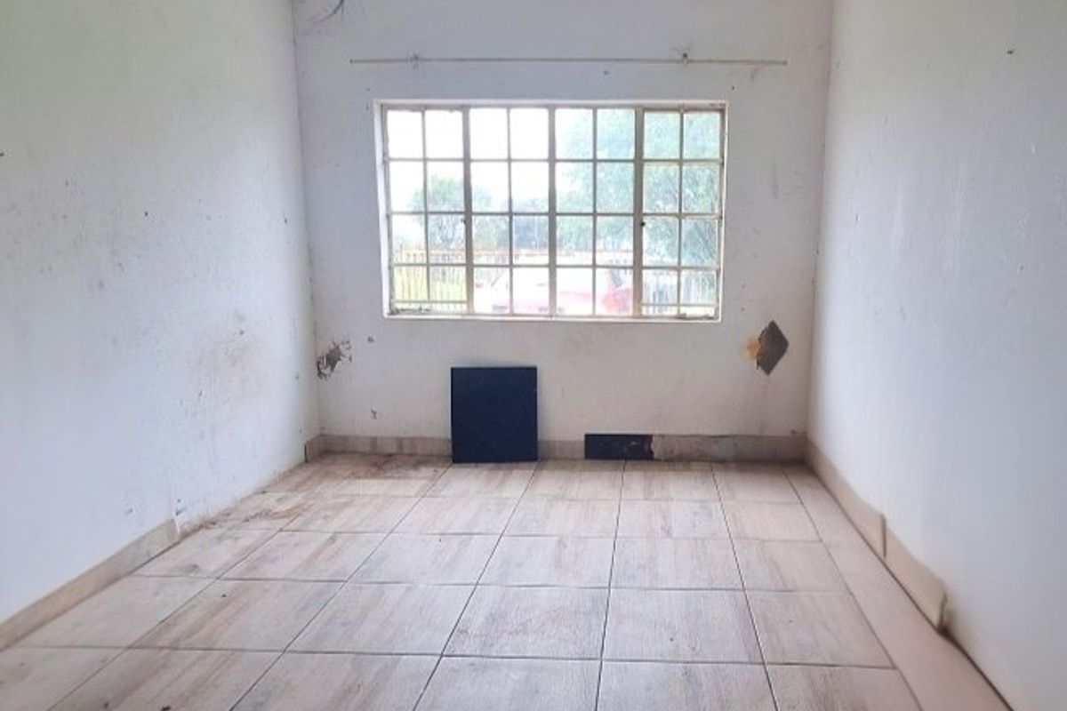 An empty bedroom featuring tiled flooring and a grid-pattern window, currently requiring wall repairs and finishing touches.