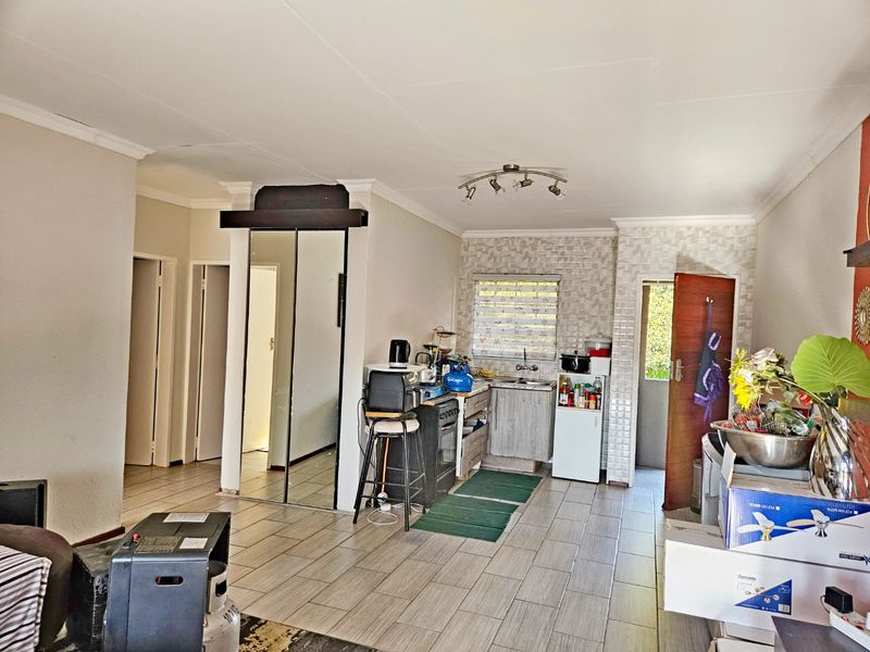 Open plan living area featuring tiled floors, a compact kitchen with textured wall tiles, and mirrored built-in storage cupboards.