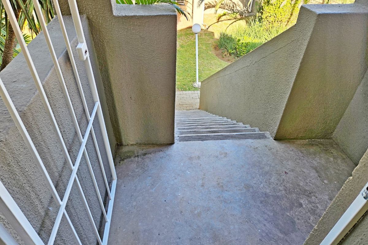 An exterior staircase leading down to a garden area, featuring concrete steps, a security gate, and paved pathways.