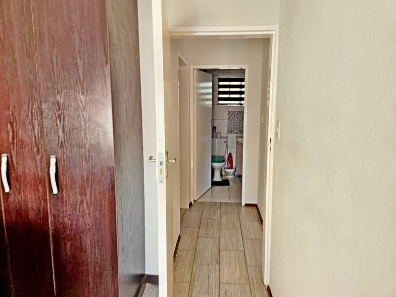 A view through a hallway featuring tiled flooring and a built-in cupboard, leading towards a bathroom.