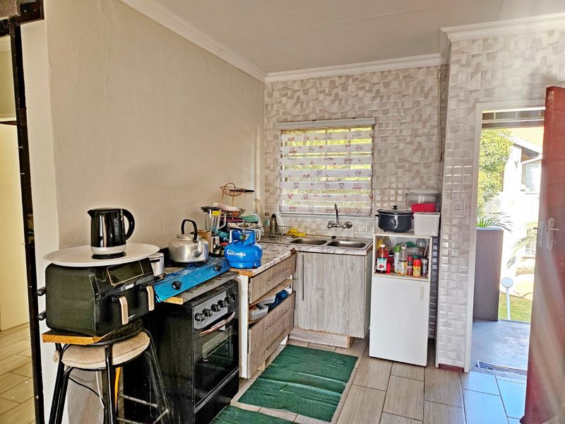 A compact kitchen area featuring a double basin sink, tiled backsplash, and built-in cabinetry, providing functional space for meal preparation.
