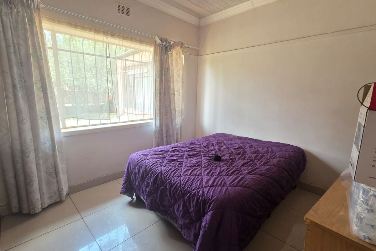 A standard bedroom featuring tiled flooring, security bars on the window, and ceiling cornicing, offering a functional space ready for cosmetic updates.