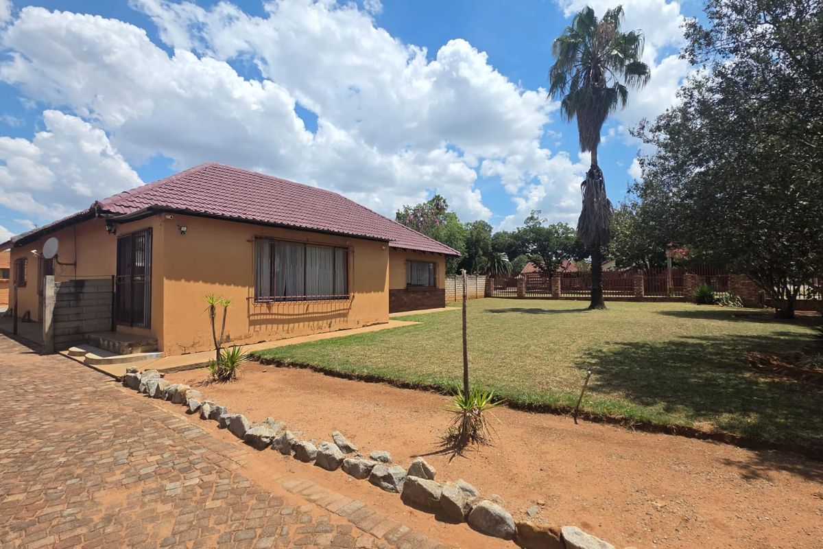 Rear view of the property featuring a tiled roof, paved driveway, and a spacious lawn area enclosed by a boundary wall.