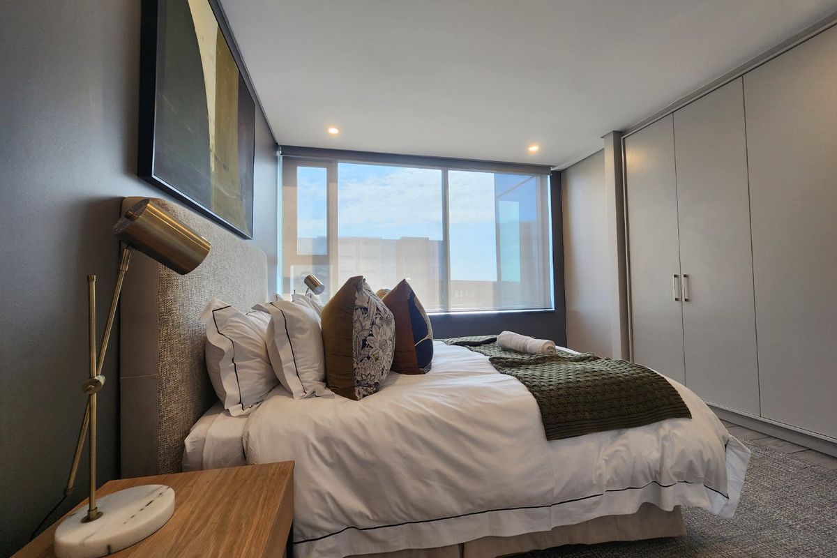 A modern bedroom featuring built-in cupboards, recessed downlighting, and large windows allowing for natural light.