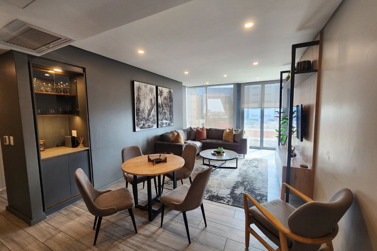Modern open-plan living and dining area featuring wood-look tile flooring, recessed lighting, built-in bar cabinetry, and large windows with natural light.