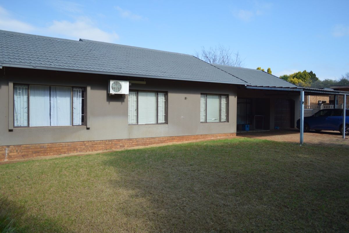 Rear view of the house featuring a tiled roof, brick base, and an attached carport area with a lawn.