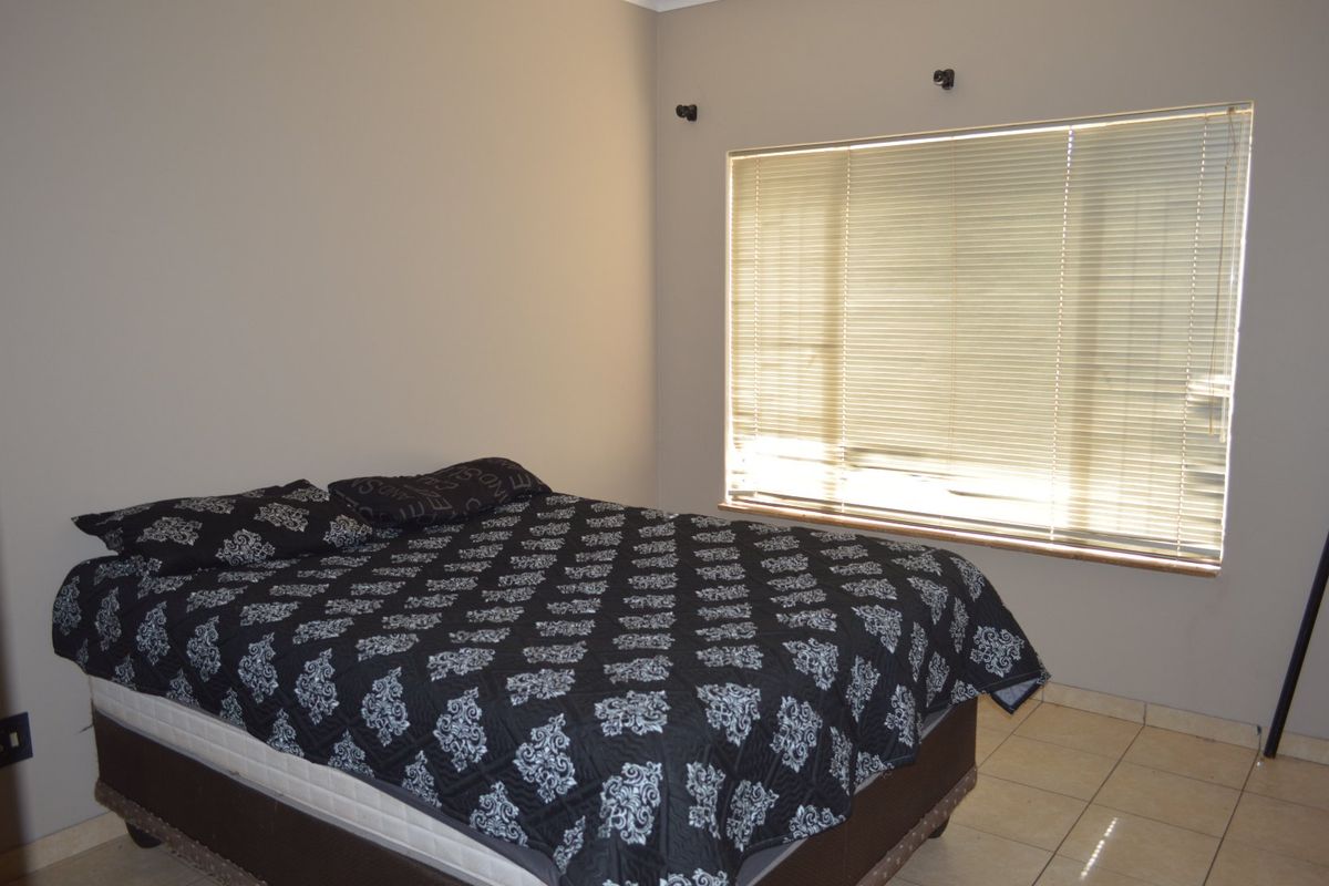 A simple bedroom featuring neutral wall tones, tiled flooring, and a large window fitted with venetian blinds.