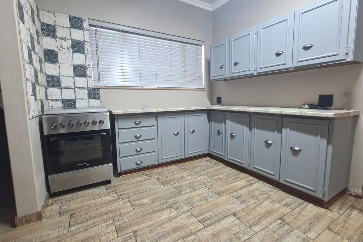 A functional kitchen featuring grey painted cabinetry, laminate countertops, a freestanding oven, and decorative tiled backsplash with wood-look ceramic floor tiles.