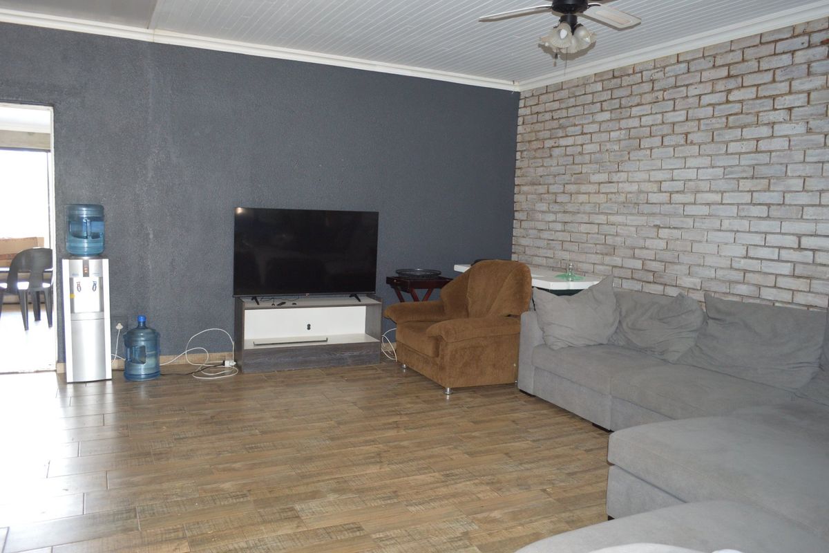 A living room featuring wood-look tiled flooring, an exposed brick feature wall, and a ceiling fan with a tongue and groove ceiling finish.