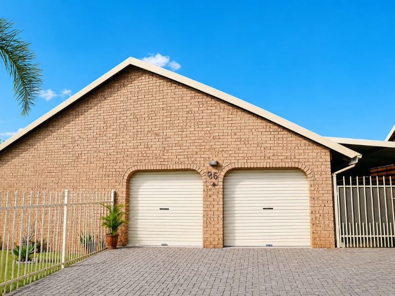 Front view of a residential property featuring a double garage with roller shutter doors, paved driveway, and secure metal perimeter fencing.