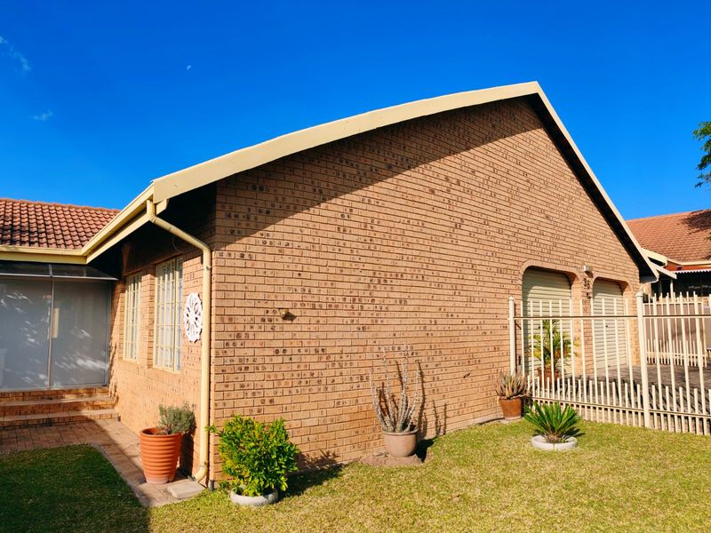 A well-maintained face brick house featuring a double garage, tiled roof, and a paved entrance walkway set within a neat garden.