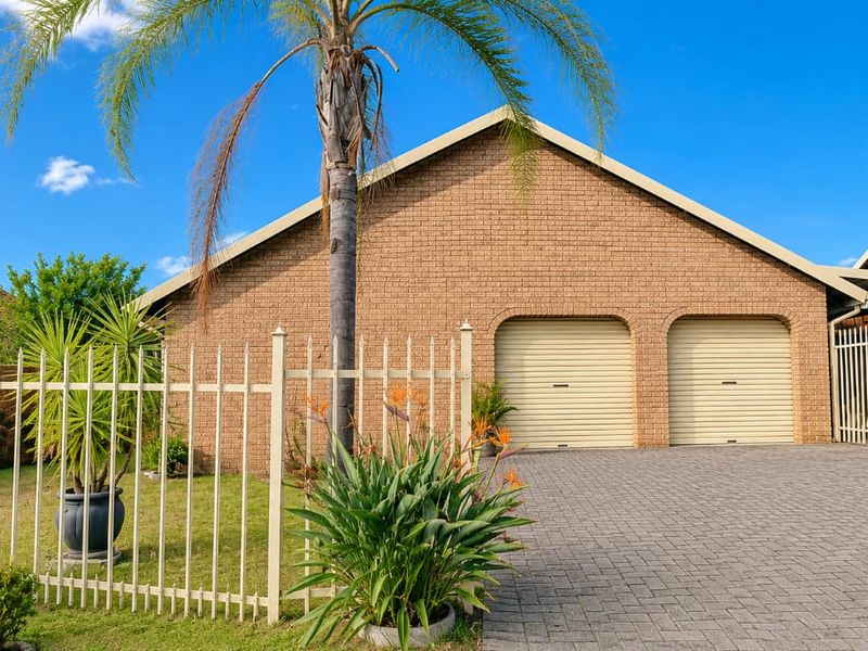 Front view of a well-maintained brick house featuring a double garage with roller doors and a paved driveway.