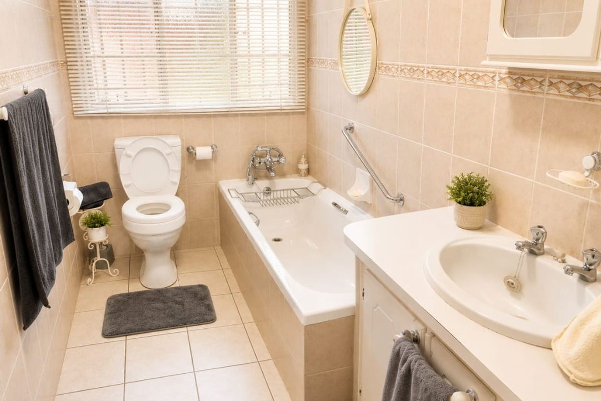 A functional bathroom featuring a built-in vanity with basin, a bathtub with shower mixer, toilet, and neutral floor-to-ceiling wall tiling.