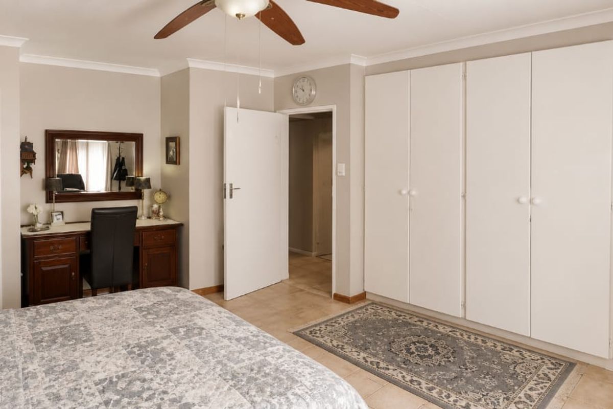 A well-maintained bedroom featuring extensive built-in cupboards, tiled flooring, a ceiling fan, and direct access to an en-suite bathroom.