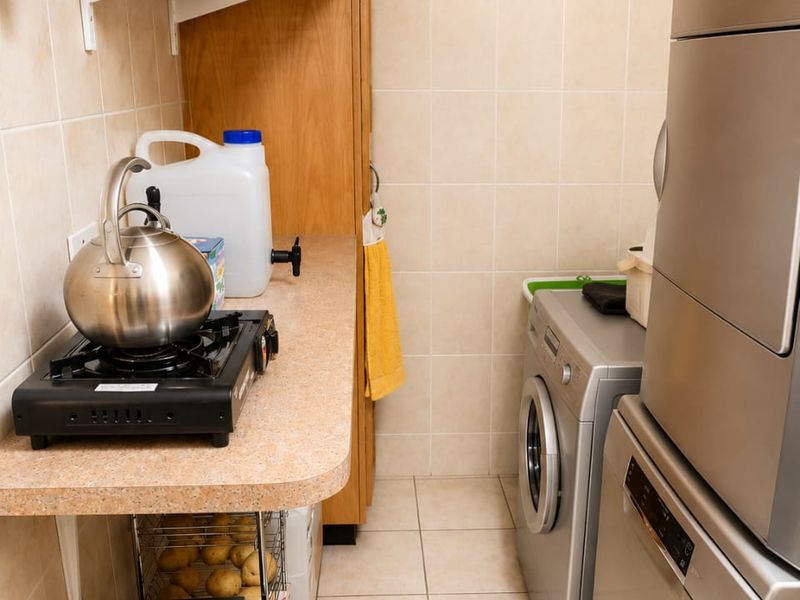 A functional laundry area featuring tiled walls and flooring, laminate countertops, and built-in cabinetry for storage and appliance integration.