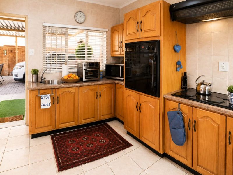 A functional kitchen featuring traditional wooden cabinetry, laminate countertops, built-in oven, electric hob, and tiled finishes with direct access to the exterior.