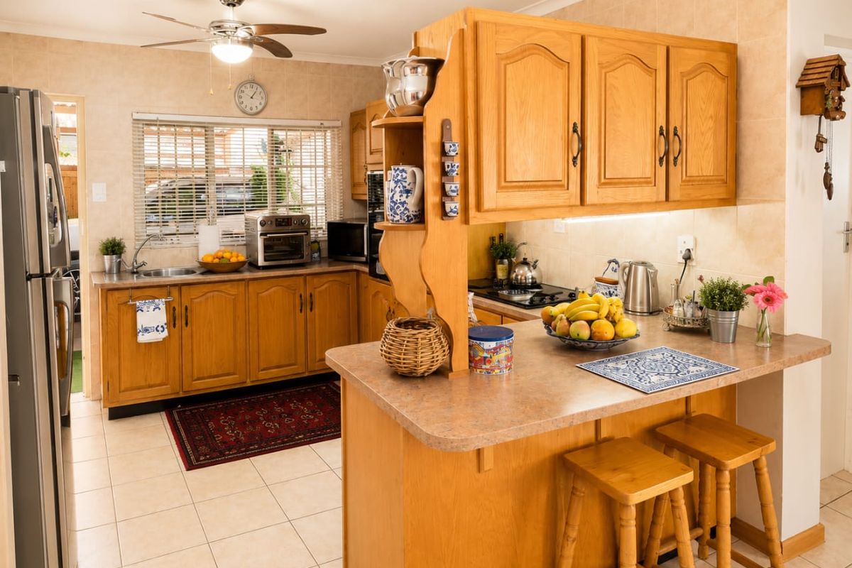 A functional kitchen featuring traditional wooden cabinetry, laminate countertops, a gas hob, and tiled flooring with a breakfast bar area.