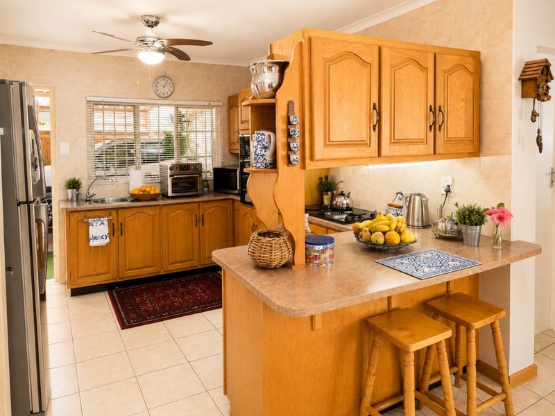 A functional kitchen featuring traditional wooden cabinetry, laminate countertops, a gas hob, and tiled flooring with a breakfast bar area.