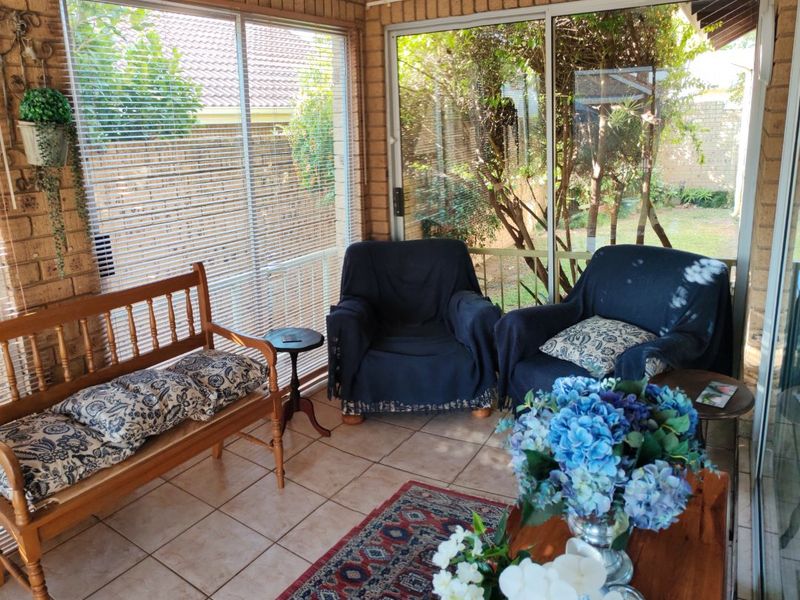 A sun-filled enclosed patio featuring exposed brick walls, ceramic tiled flooring, and large sliding glass doors providing views of the garden.