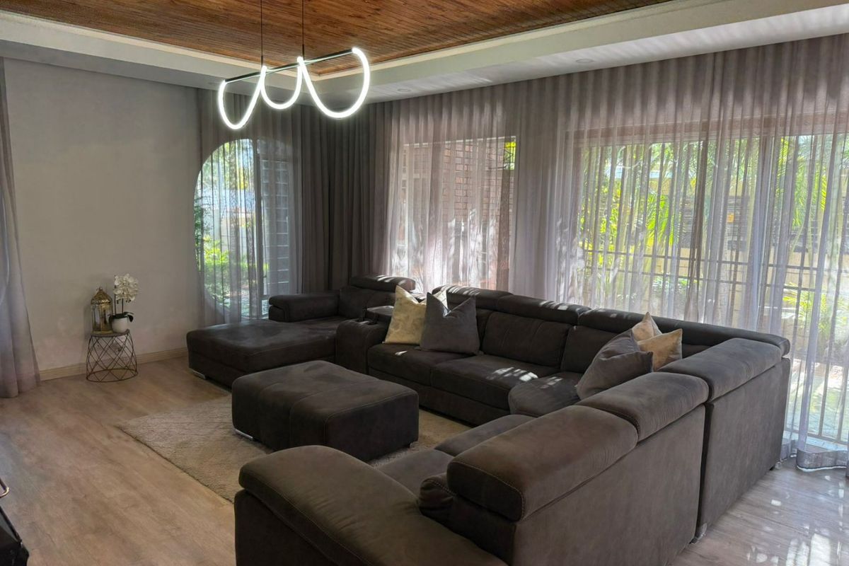 Spacious living room featuring a warm timber-clad ceiling, modern pendant lighting, and large windows that provide ample natural light and garden views.