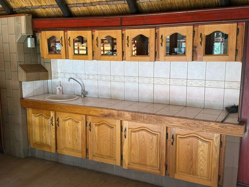 Outdoor entertainment area featuring a thatched roof, built-in wooden cabinetry, tiled countertop, and a sink, ideal for alfresco dining and hosting.