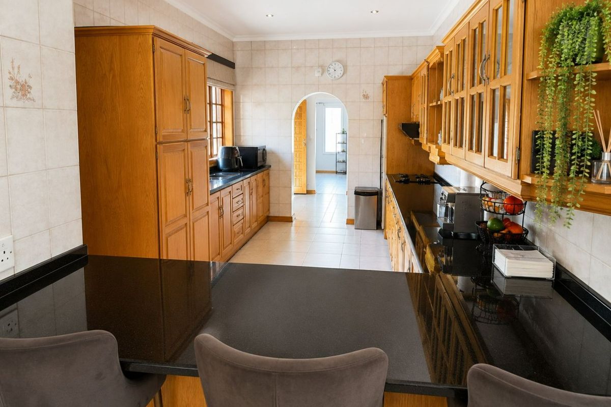 A functional kitchen featuring traditional wooden cabinetry, dark granite countertops, and a tiled backsplash, leading through an archway to an adjacent space.