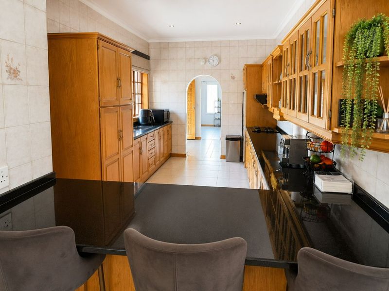 A functional kitchen featuring traditional wooden cabinetry, dark granite countertops, and a tiled backsplash, leading through an archway to an adjacent space.