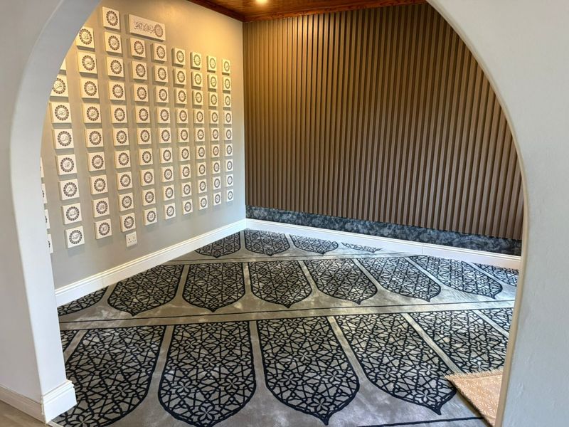 A dedicated prayer room featuring custom patterned carpeting, slatted timber wall paneling, and decorative wall tiles framed by an elegant arched entryway.