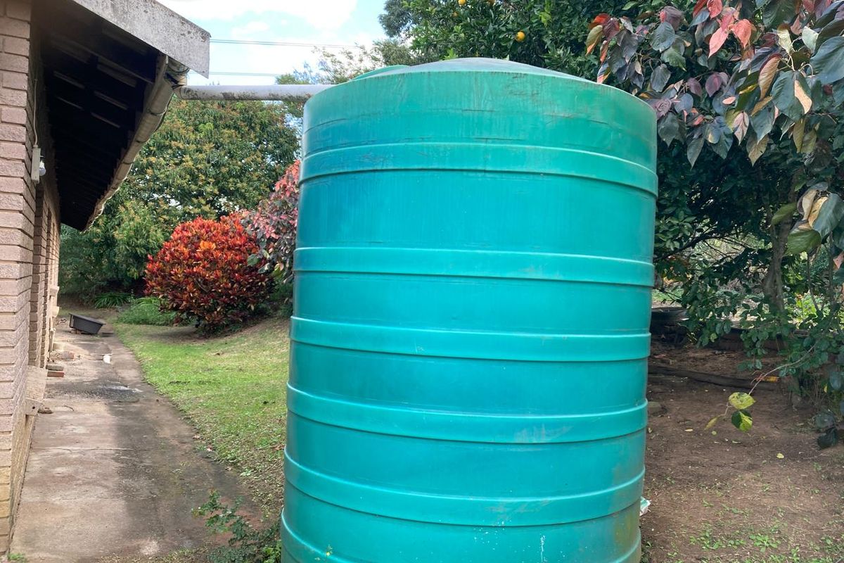 A rear exterior view showing a large green water storage tank connected to the house guttering system, situated on a concrete path.