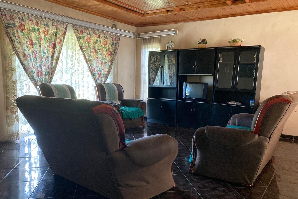 A living room featuring dark tiled flooring and a timber-paneled ceiling, offering a dated aesthetic that could be modernized with updated finishes.