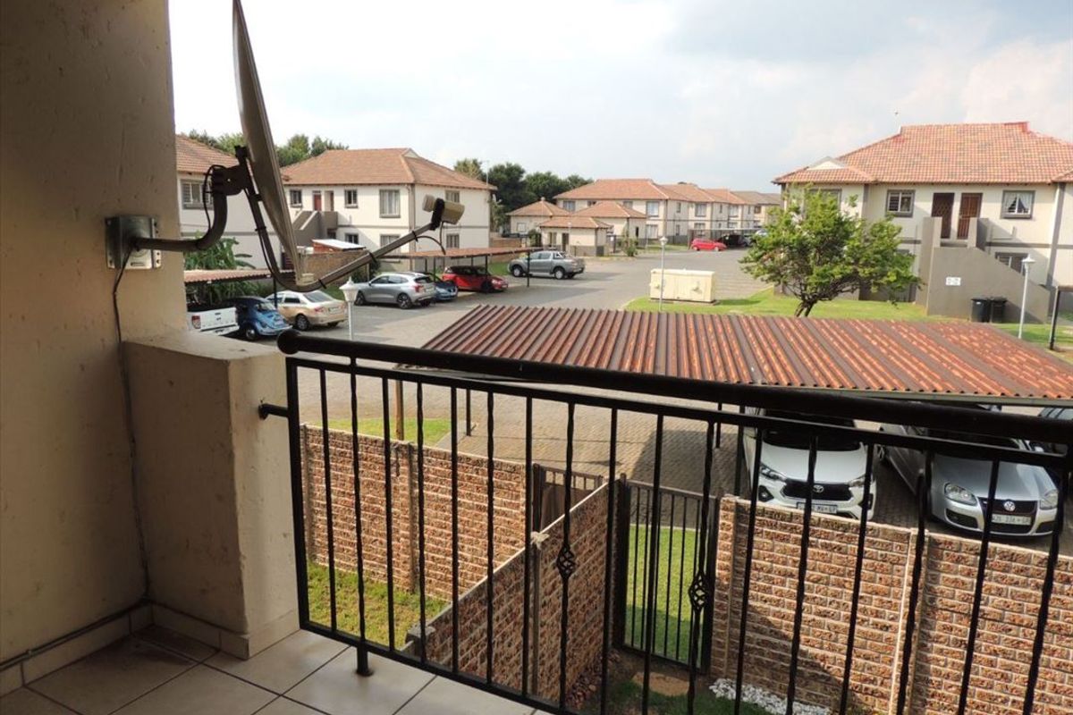 A covered balcony overlooking the complex parking area, featuring tiled flooring and a metal balustrade.