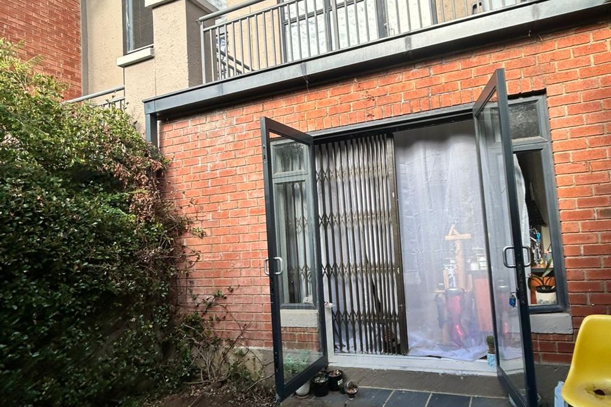 Rear exterior view of a townhouse featuring a brick facade, a small balcony with metal railings, and double glass doors leading to a garden area.