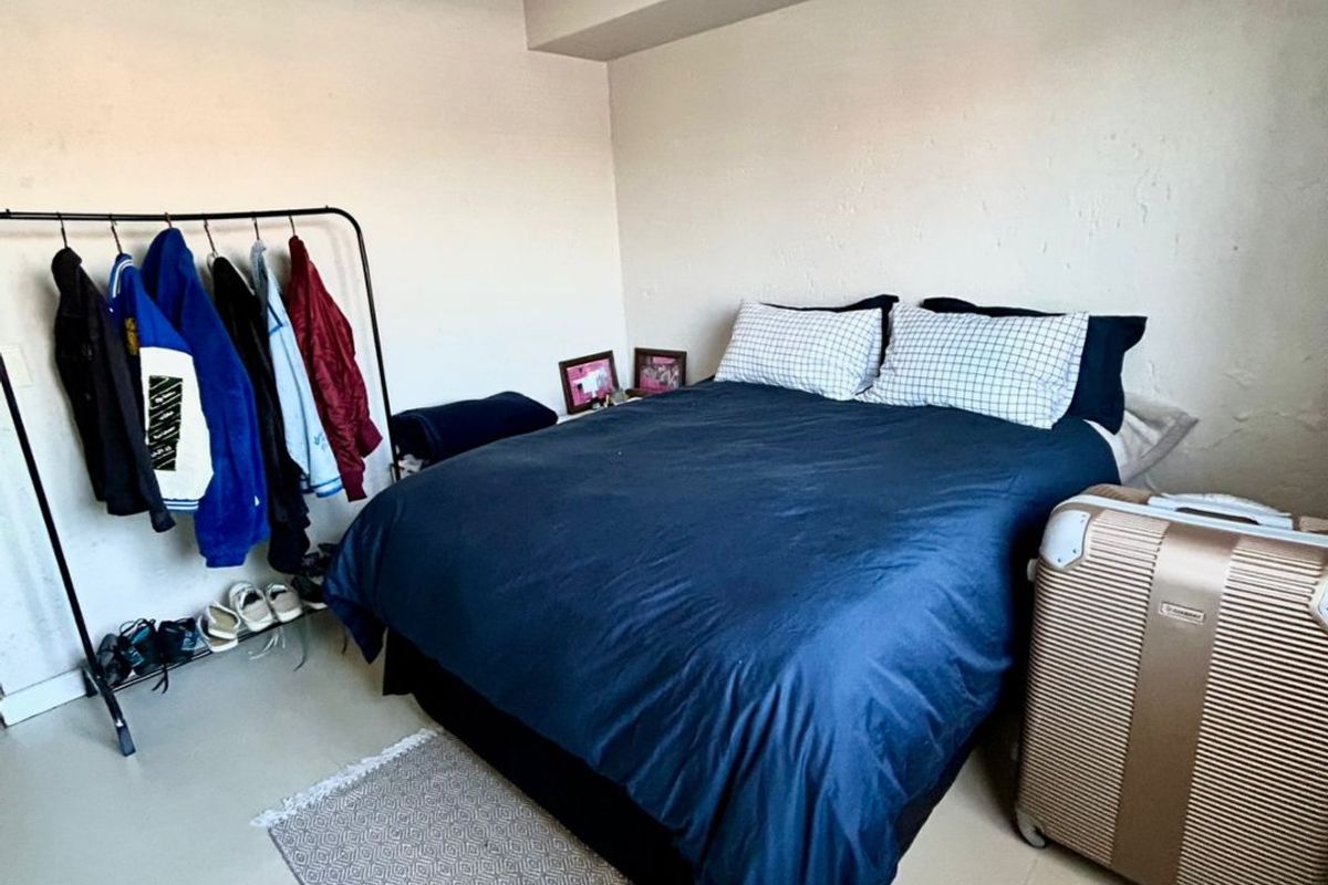 A bedroom featuring tiled flooring and a central pendant light fixture, with visible wall plaster imperfections.
