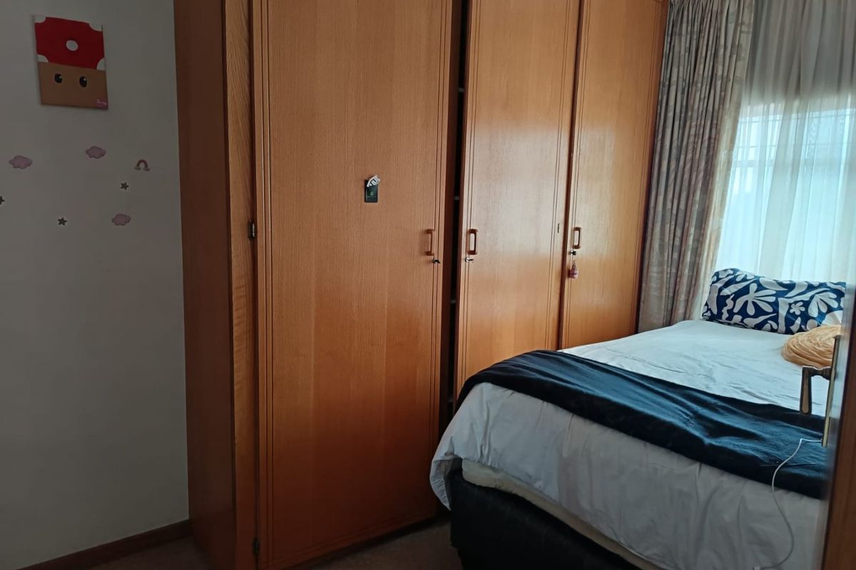 A bedroom featuring a large, floor-to-ceiling built-in wooden wardrobe and window with curtain treatments.