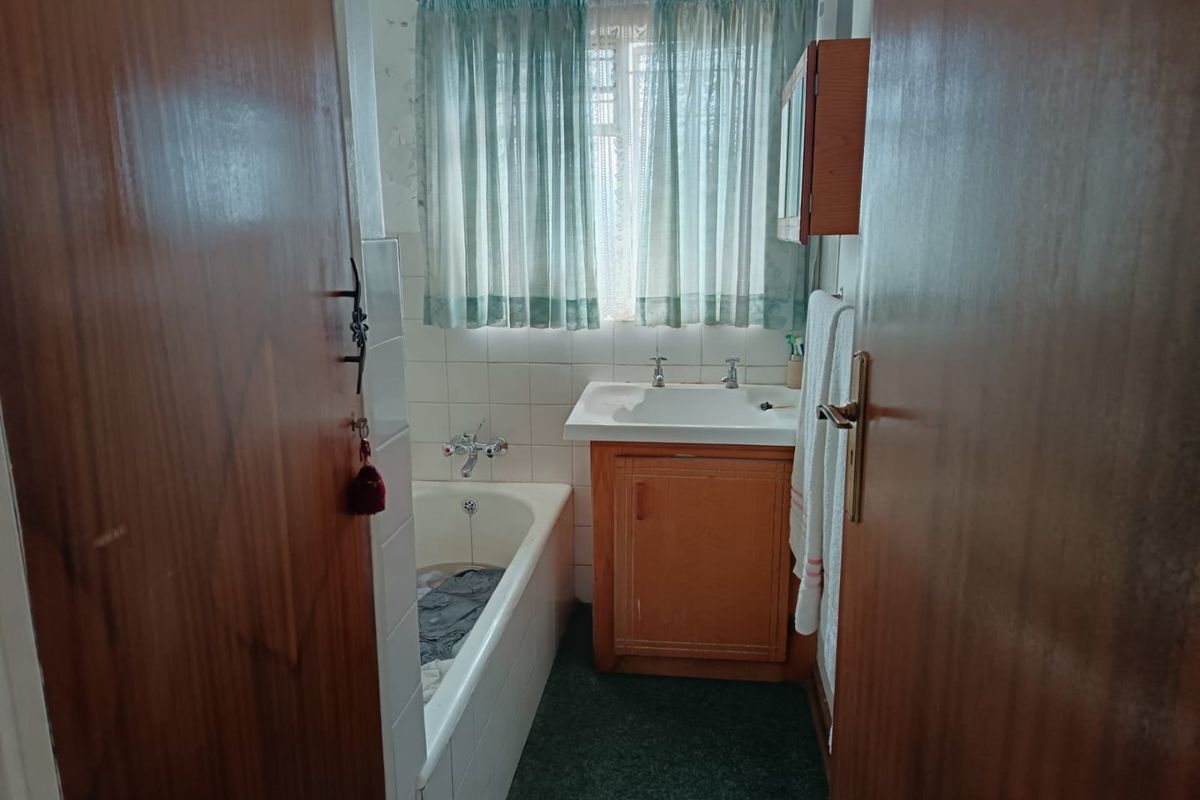 A dated bathroom featuring a built-in vanity, bathtub, and tiled splashback, currently showing signs of wear and requiring cosmetic updates.
