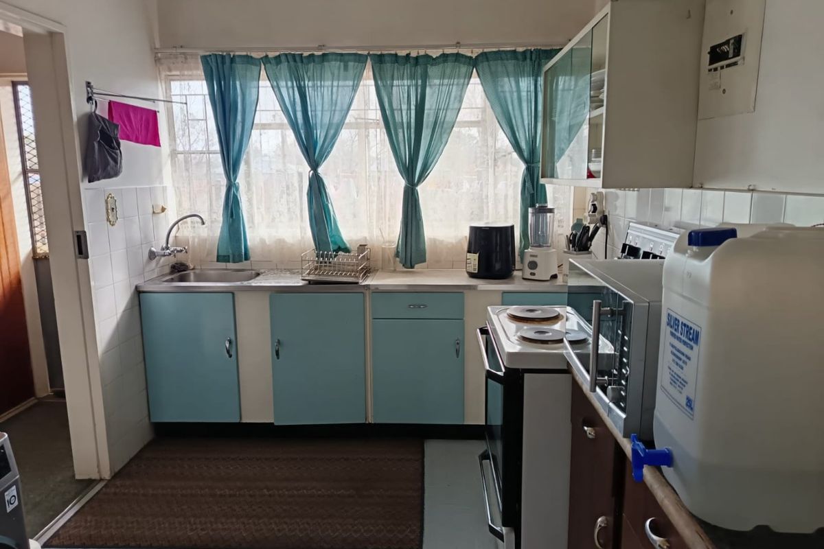 A functional kitchen featuring original cabinetry, a stainless steel sink, and a tiled splashback, offering potential for a modern renovation.