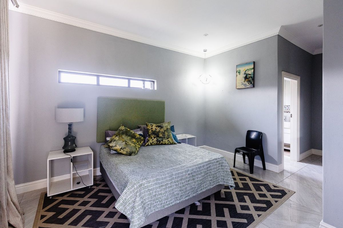 A well-maintained bedroom featuring neutral grey walls, crown molding, tiled flooring, and a high-positioned clerestory window for natural light.