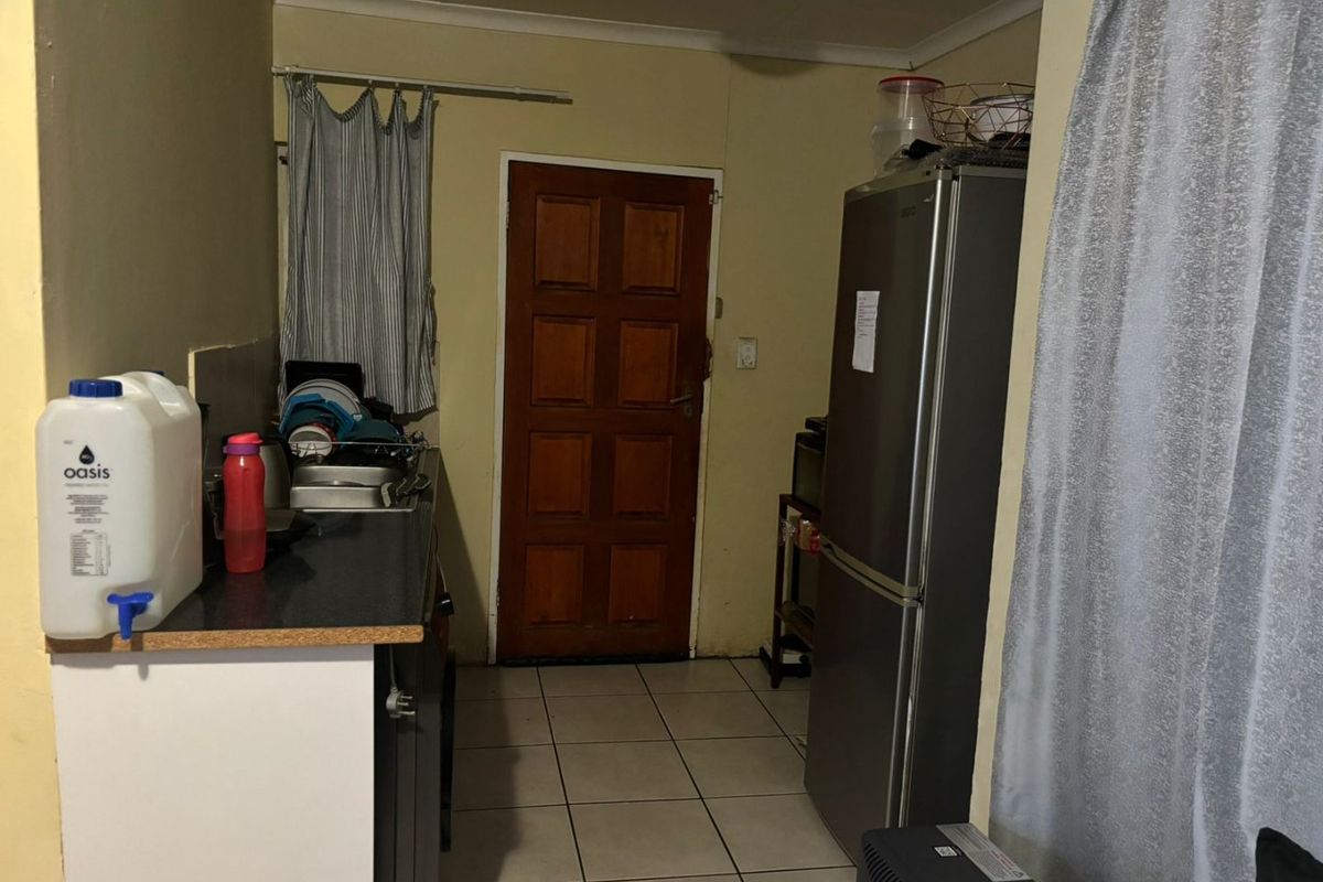 A compact kitchen area featuring tiled flooring, a laminate countertop with a stainless steel sink, and a timber door leading to the exterior.