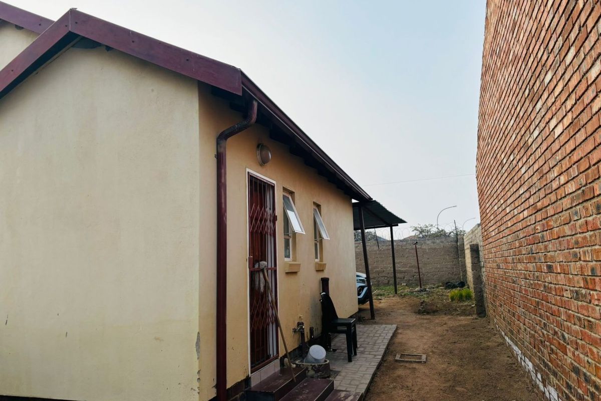 Rear exterior view of the property showing a paved walkway, security gate, and basic wall finishes along the side of the house.