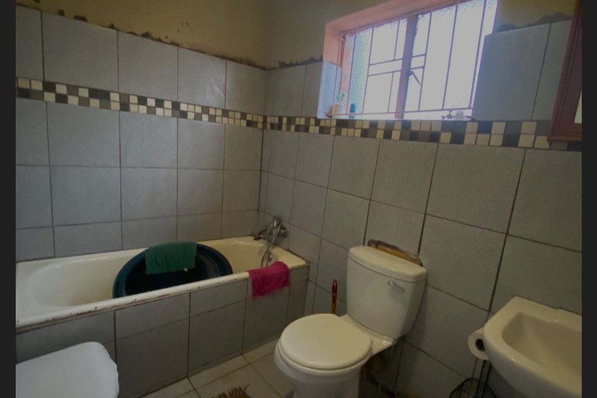 A dated bathroom featuring a bathtub, pedestal basin, and toilet, requiring significant cosmetic updates and tile repairs to improve its condition.