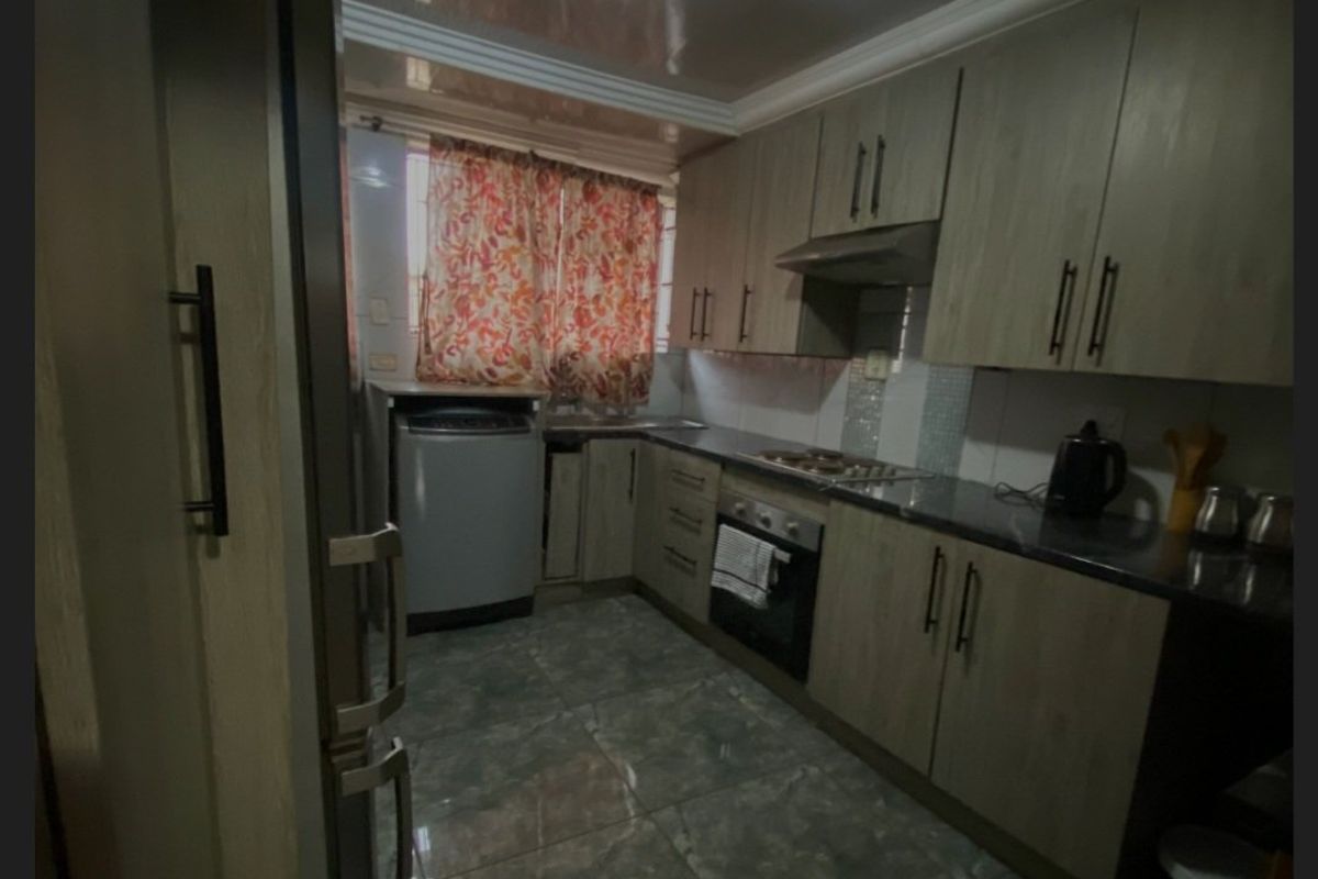 A functional kitchen featuring wood-finish cabinetry, stone countertops, integrated oven and hob, and tiled flooring.